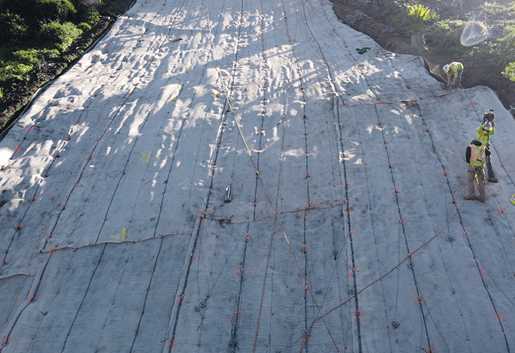 Construction site featuring a textured, gray surface with orange markings, where workers are engaged in installation tasks under bright lighting.
